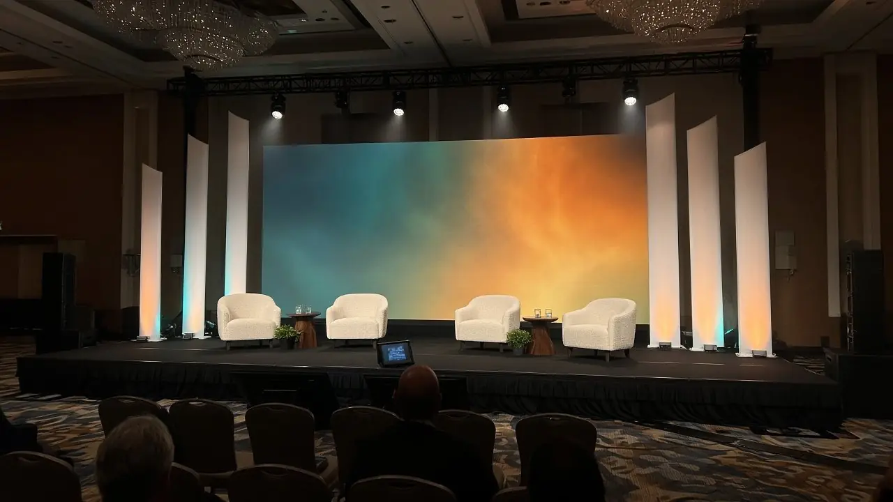 Concept render of a general session stage with white armchairs and angled white fins around a large screen